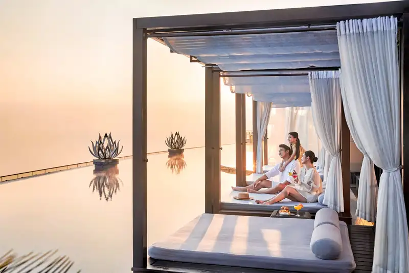 Gia đình ngồi trong cabana rèm trắng bên hồ vô cực lúc bình minh