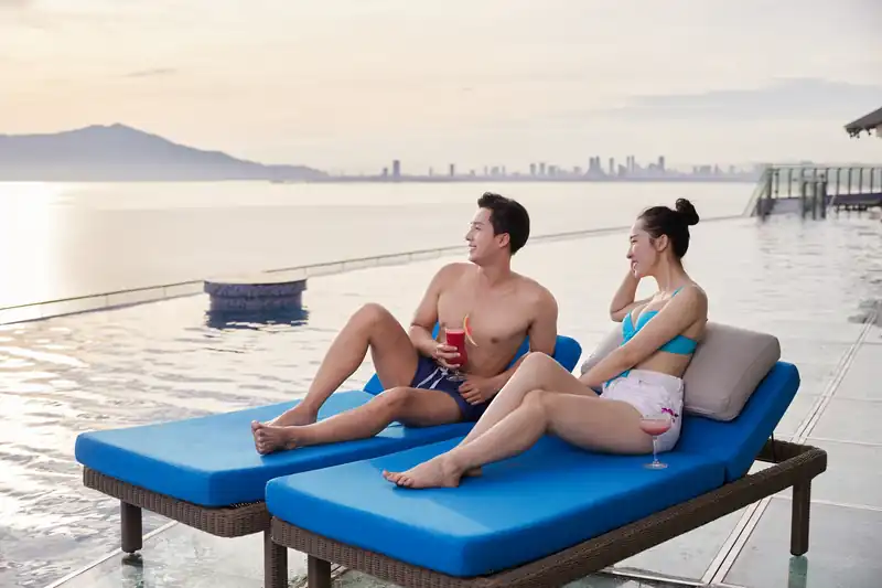 Cặp đôi nằm ghế tắm nắng bên hồ vô cực tầng 22, phía xa là thành phố Đà Nẵng