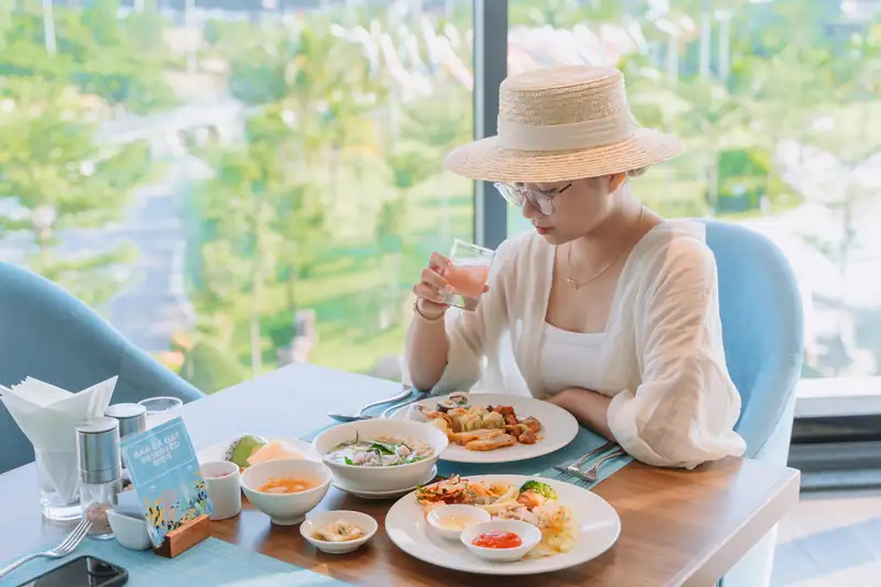 Khách ăn sáng bên cửa kính nhìn ra vườn ở nhà hàng The Blue