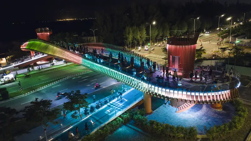 Cầu đi bộ lượn sóng phát đèn nhiều màu băng qua đường ven biển lúc tối, trước Mikazuki Đà Nẵng