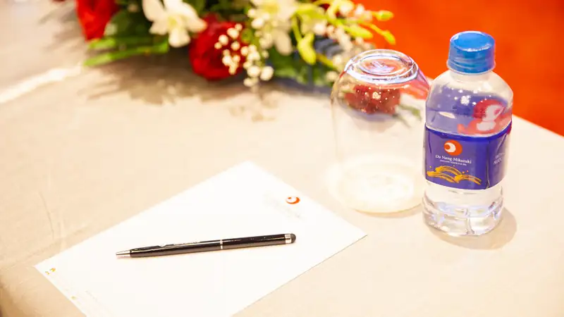 Bàn hội nghị phủ khăn trắng với sổ ghi chép, bút, ly và chai nước suối in logo Da Nang Mikazuki