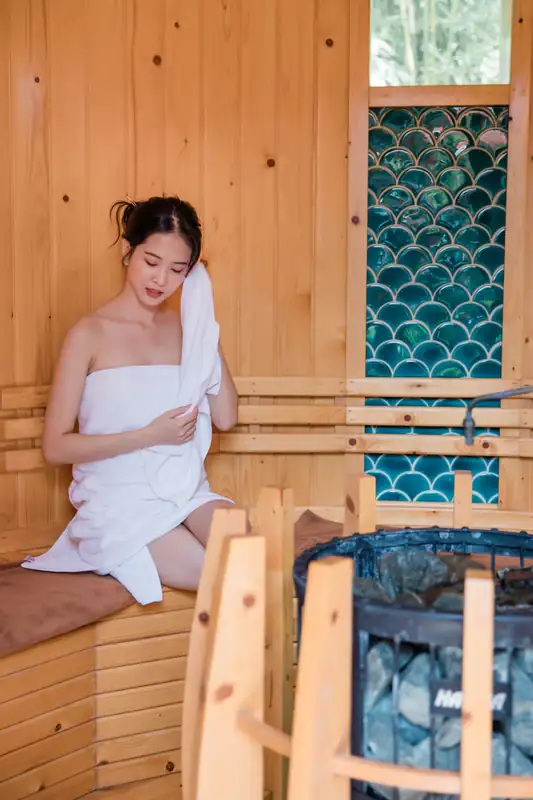 Khách quấn khăn trắng ngồi trên ghế gỗ cạnh bếp đá nóng trong phòng xông hơi khô, khu onsen Mikazuki Đà Nẵng