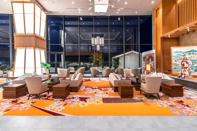Sảnh khách sạn Mikazuki Đà Nẵng với sofa, thảm hoa văn hoa anh đào, đèn lồng giấy và tranh Nhật khổ lớn bên vách kính