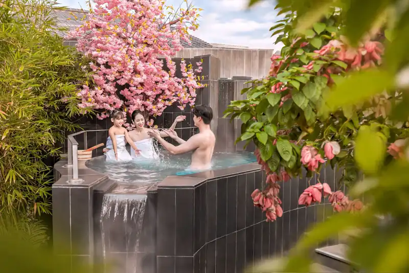 Gia đình ngâm bể onsen tròn có thác nước nhỏ giữa cây hoa anh đào, Mikazuki Đà Nẵng