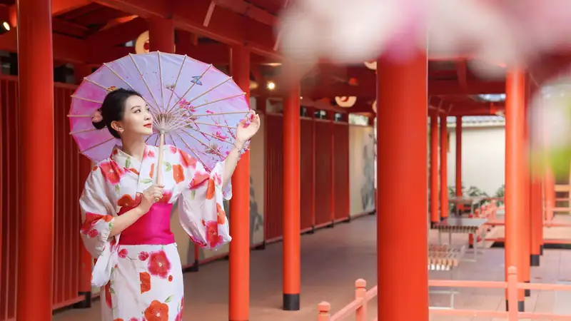Khách mặc yukata hoa đỏ cầm dù giấy dưới hành lang cột đỏ khu onsen, Mikazuki Đà Nẵng