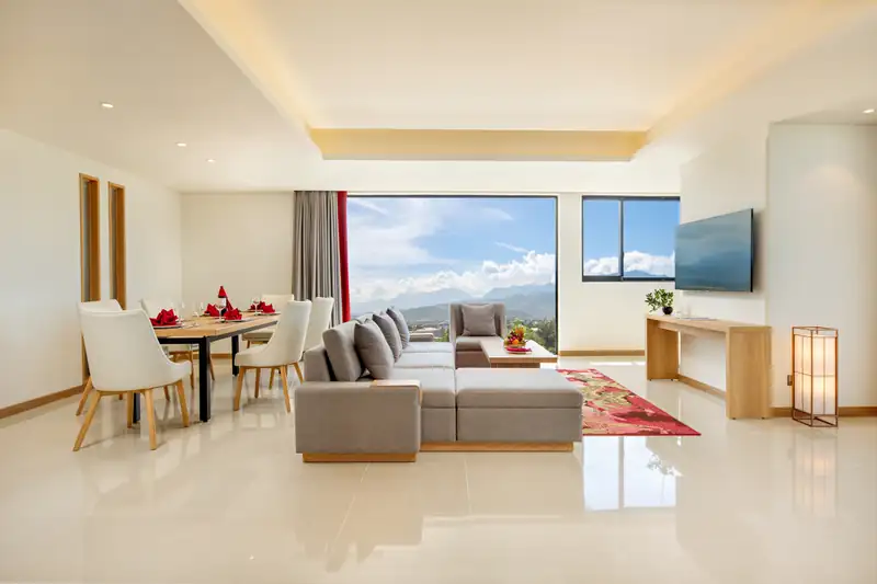 Bàn ăn 6 ghế và sofa trong phòng khách Executive Suite, cửa kính nhìn núi và biển