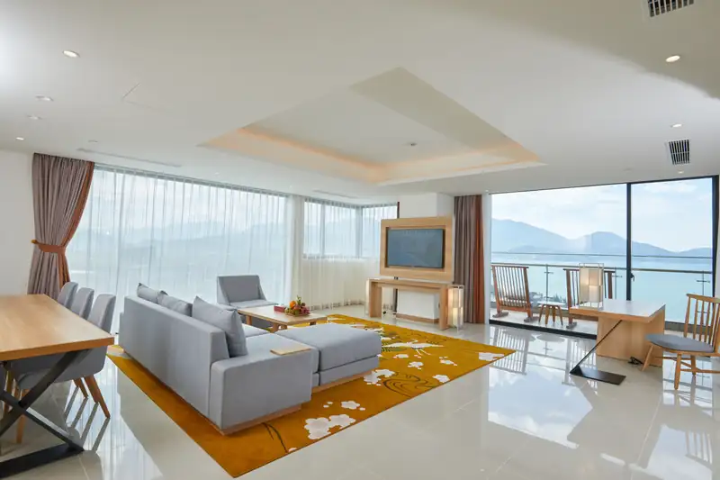 Phòng khách sofa xám và bàn ăn trong Executive Suite, cửa kính nhìn núi và biển Đà Nẵng