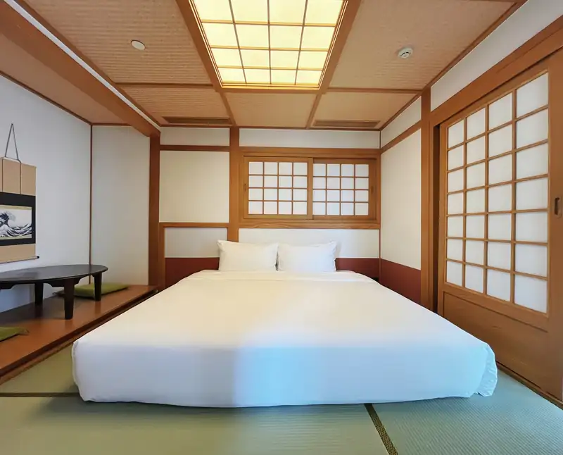 Giường đôi trên sàn tatami dưới đèn trần ô gỗ, phòng ngủ Japanese Suite
