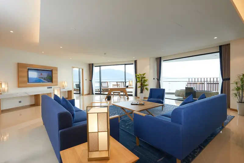 Phòng khách Presidential Suite với sofa xanh, đèn giấy kiểu Nhật và cửa kính nhìn biển