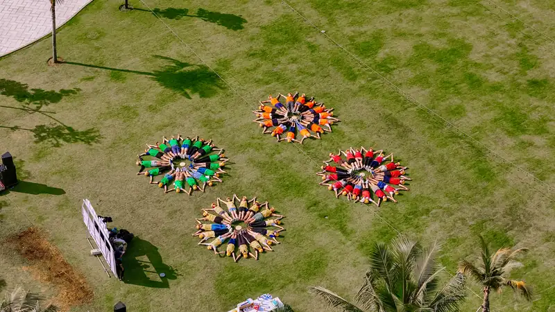 Các đội team building ngồi thành vòng tròn trên bãi cỏ, nhìn từ trên cao
